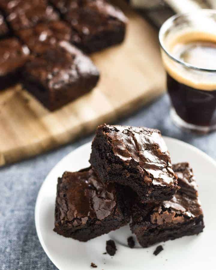 Moist chewy cocoa brownies on a plate. One with a bite out of it. Cup of coffee and board with cut brownies in background