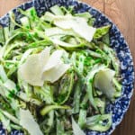 Asparagus salad in a blue and white bowl garnished with parmesan shavings.