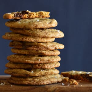 A tall stack of cookies. The top one is broken in half and the other half is on the board beside the stack.