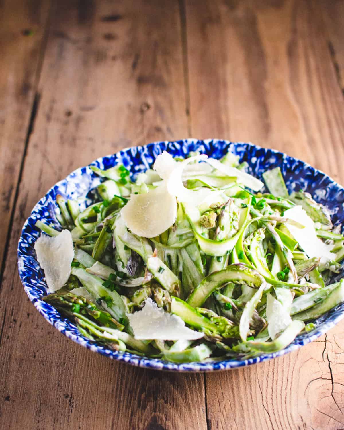 Asparagus salad in a blue and white dish garnished with shaved parmesan.