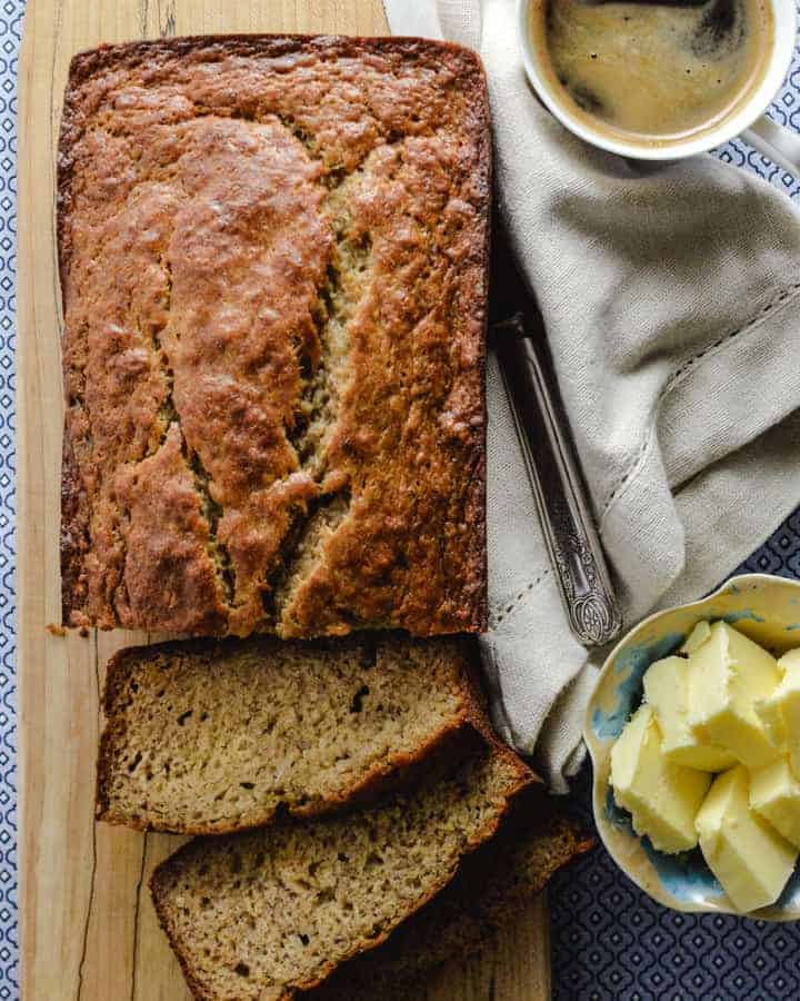 Loaf of banana bread sliced with coffee, butter, napkin and a knife