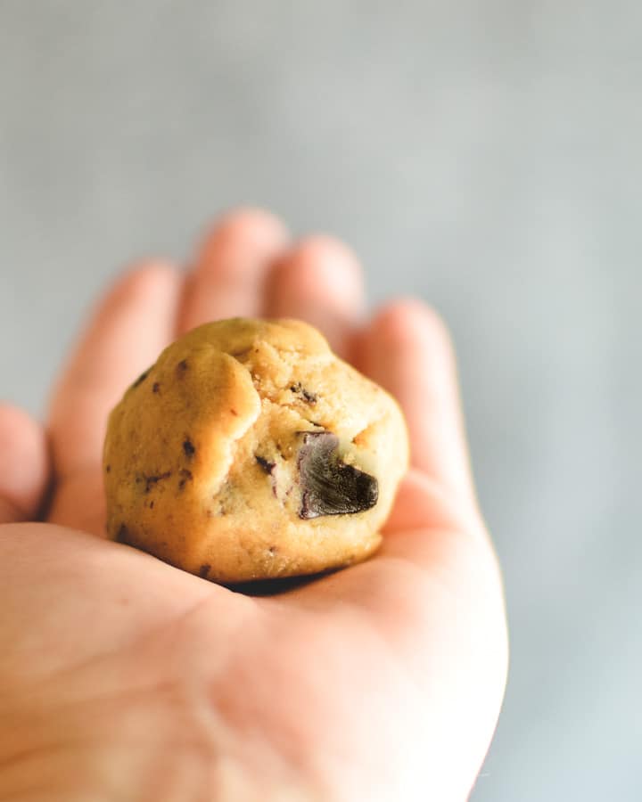 A ball of raw cookie dough in hand to show size
