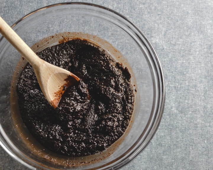 grainy looking chewy cocoa brownie mix before adding eggs with wooden spoon in glass bowl