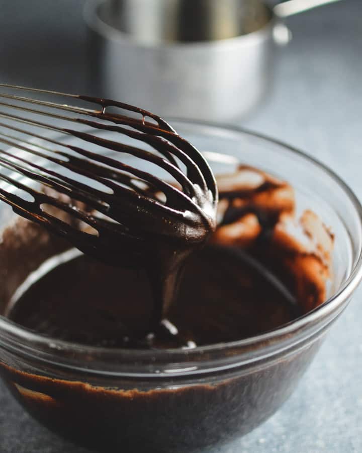 Cocoa brownie batter dripping off of a whisk into glass bowl.