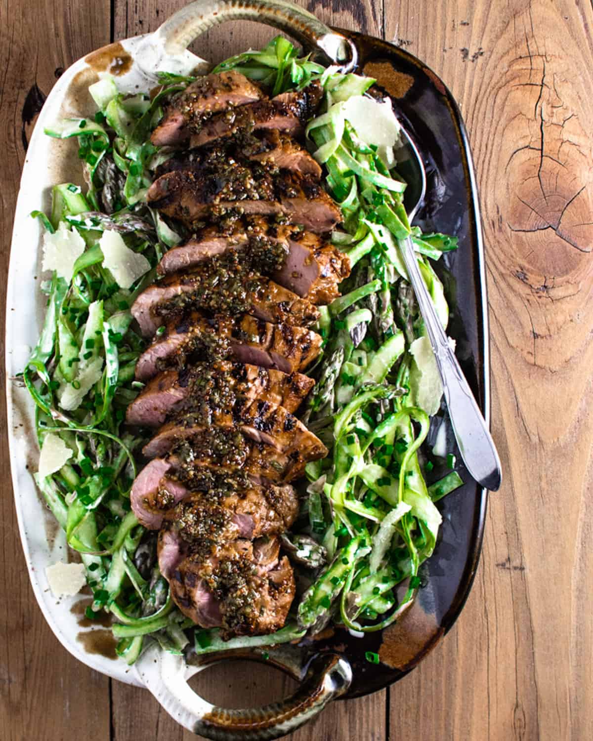 Sliced pork tenderloin on a bed of shaved asparagus salad and a serving spoon on the side.