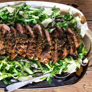 sliced pork tenderloin on a dark ceramic platter with shaved asparagus salad.