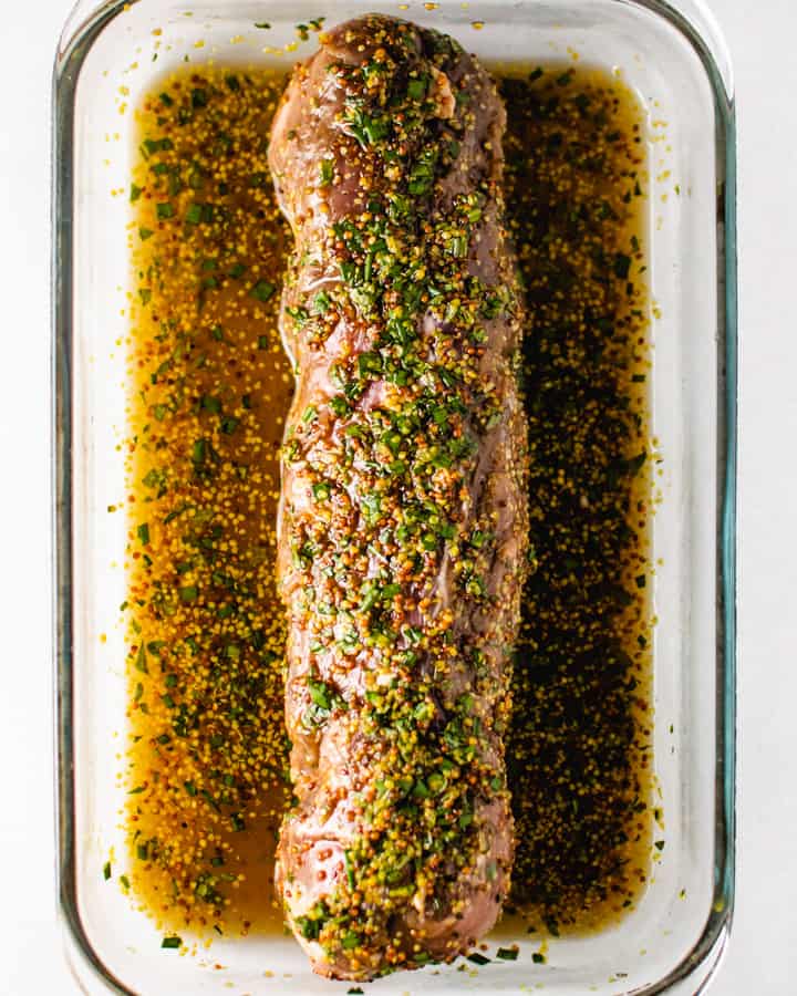 Raw pork tenderloin covered and sitting in marinade in rectangle glass dish