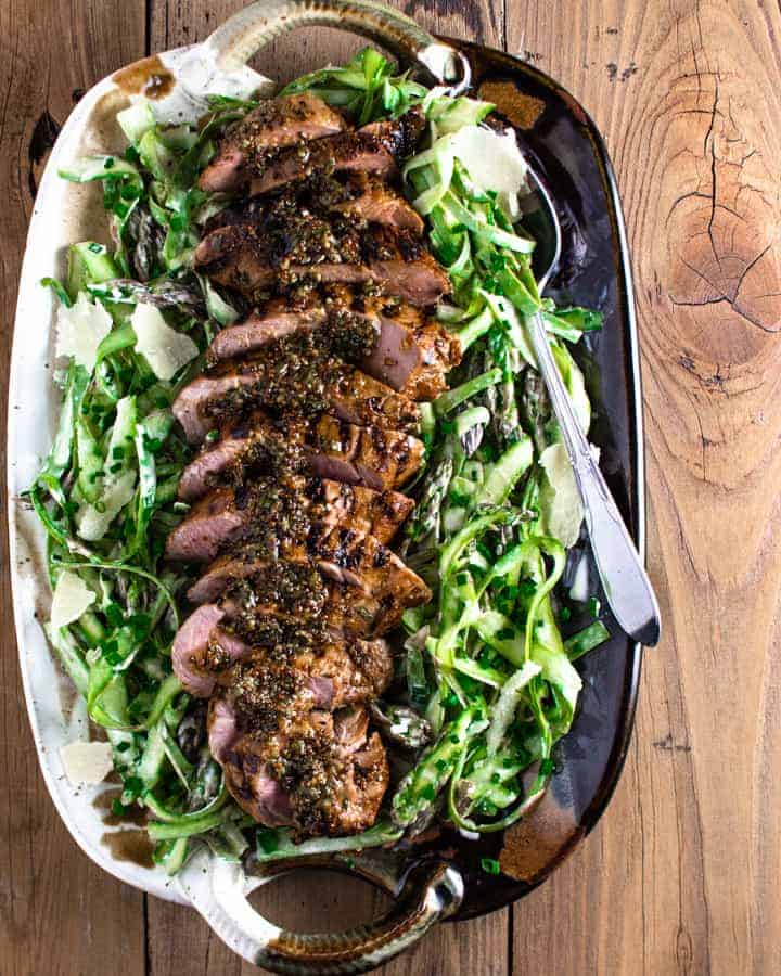 Sliced grilled pork tenderloin on a bed of shaved asparagus salad on a ceramic platter