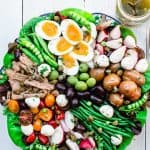 Nicoise salad with mixed vegetables, olives, tuna, boiled eggs with a dressing on the side on a round platter