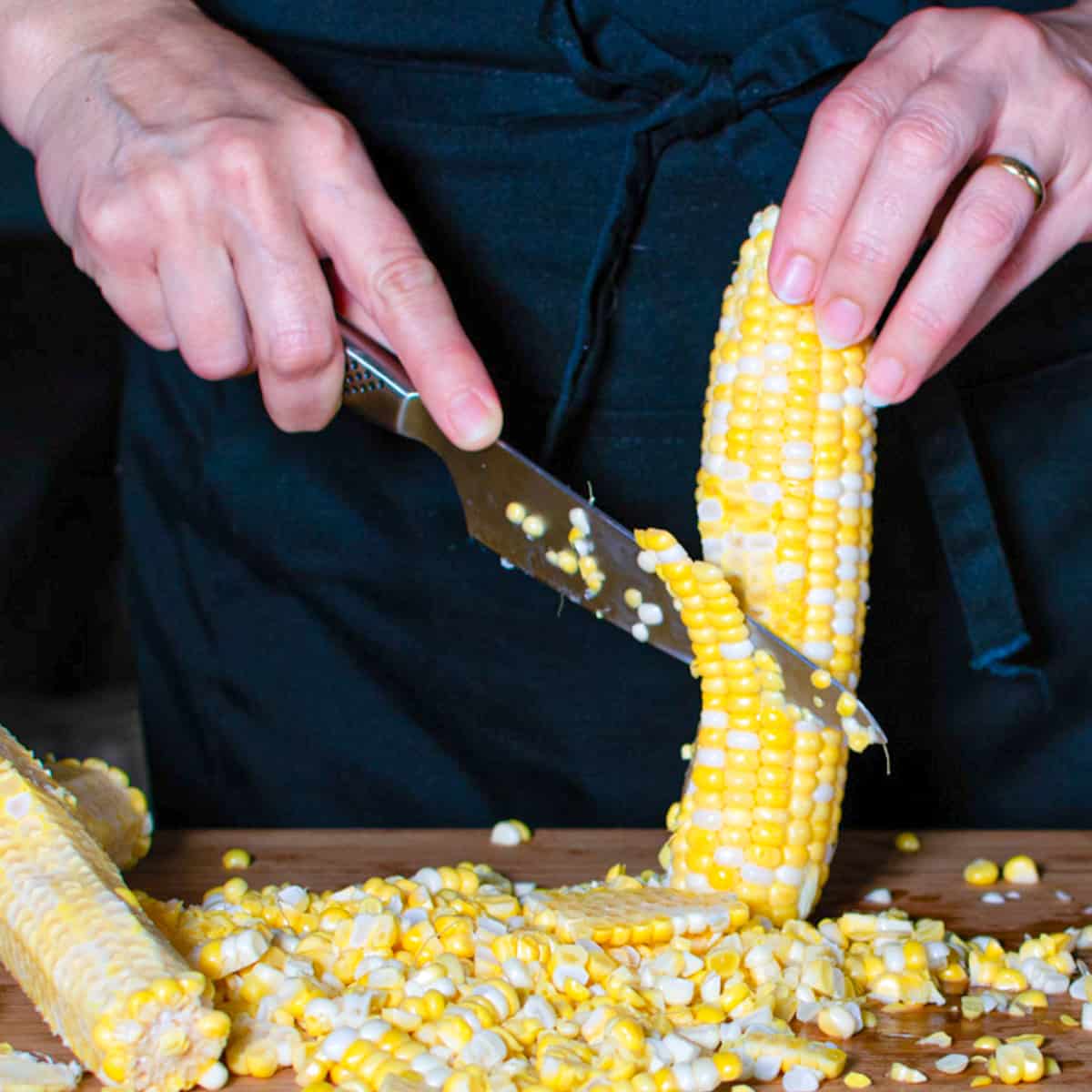 Corn being cut off the cob with a sharp knife.