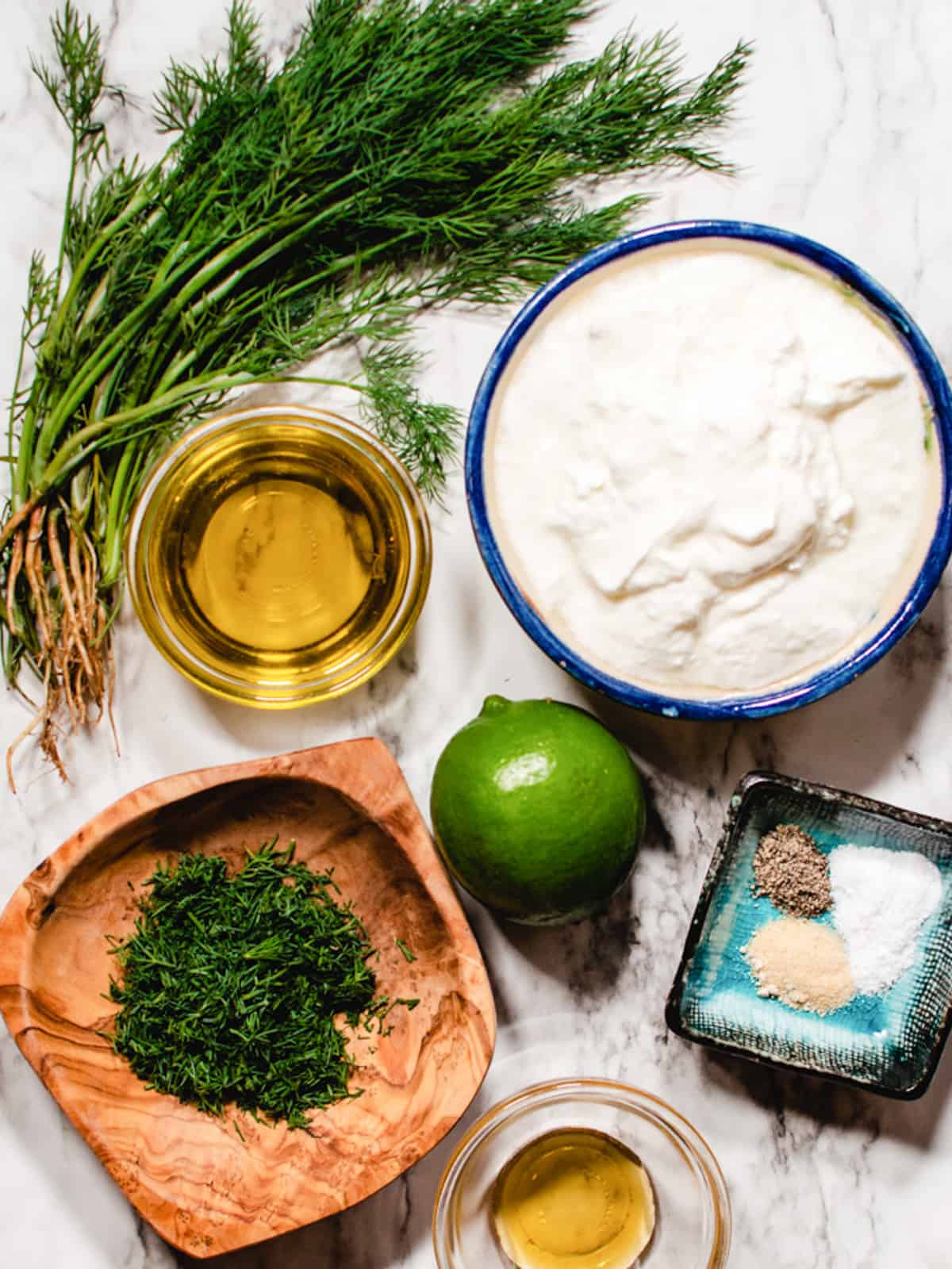 Ingredients for creamy dill dressing on a marble background.