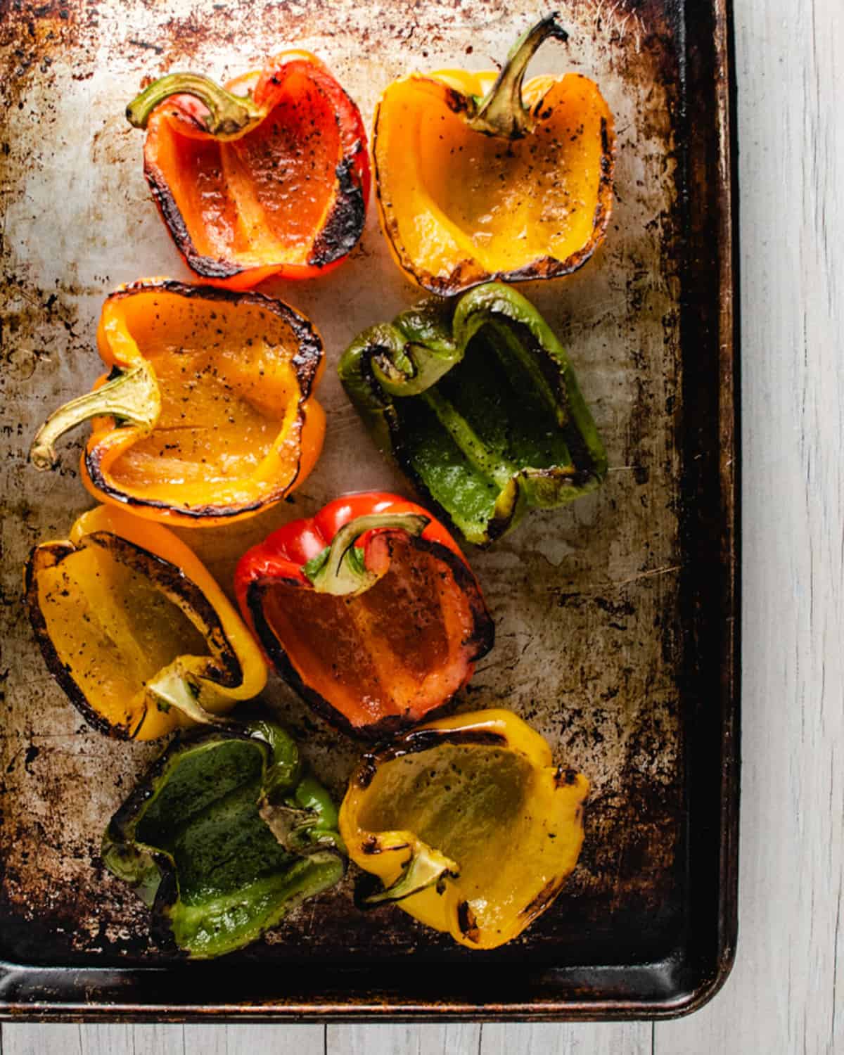 Charred peppers cut in half on a baking tray.