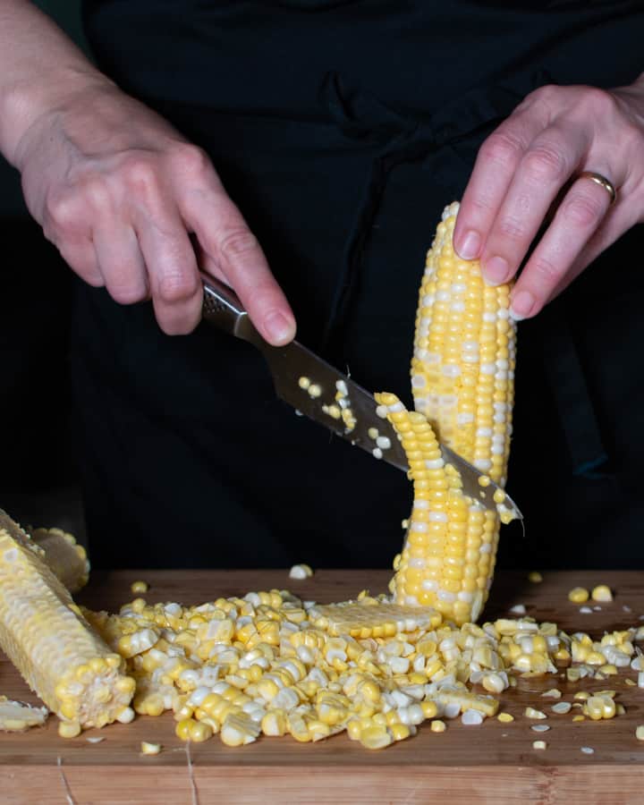 Corn being cut off the cob with a sharp knife