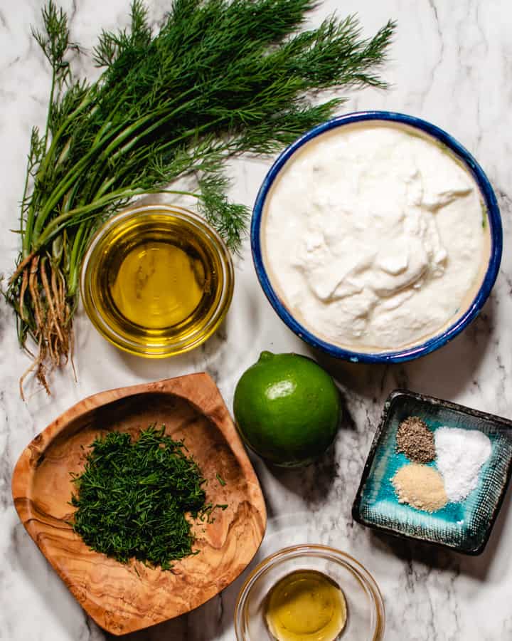 Ingredients for creamy dill dressing on a marble background
