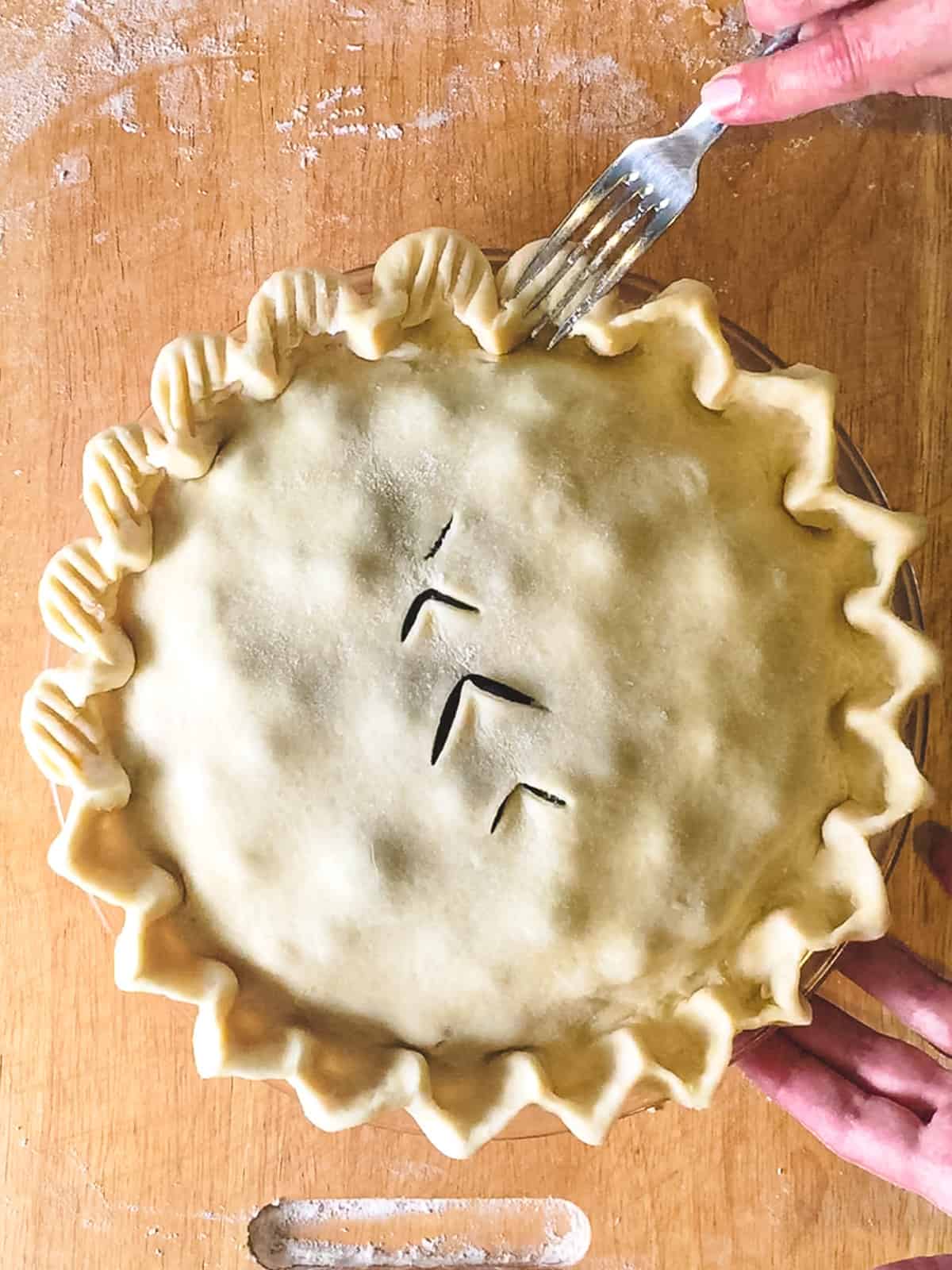 An unbaked double crust pie being forked on the edges for decoration. 