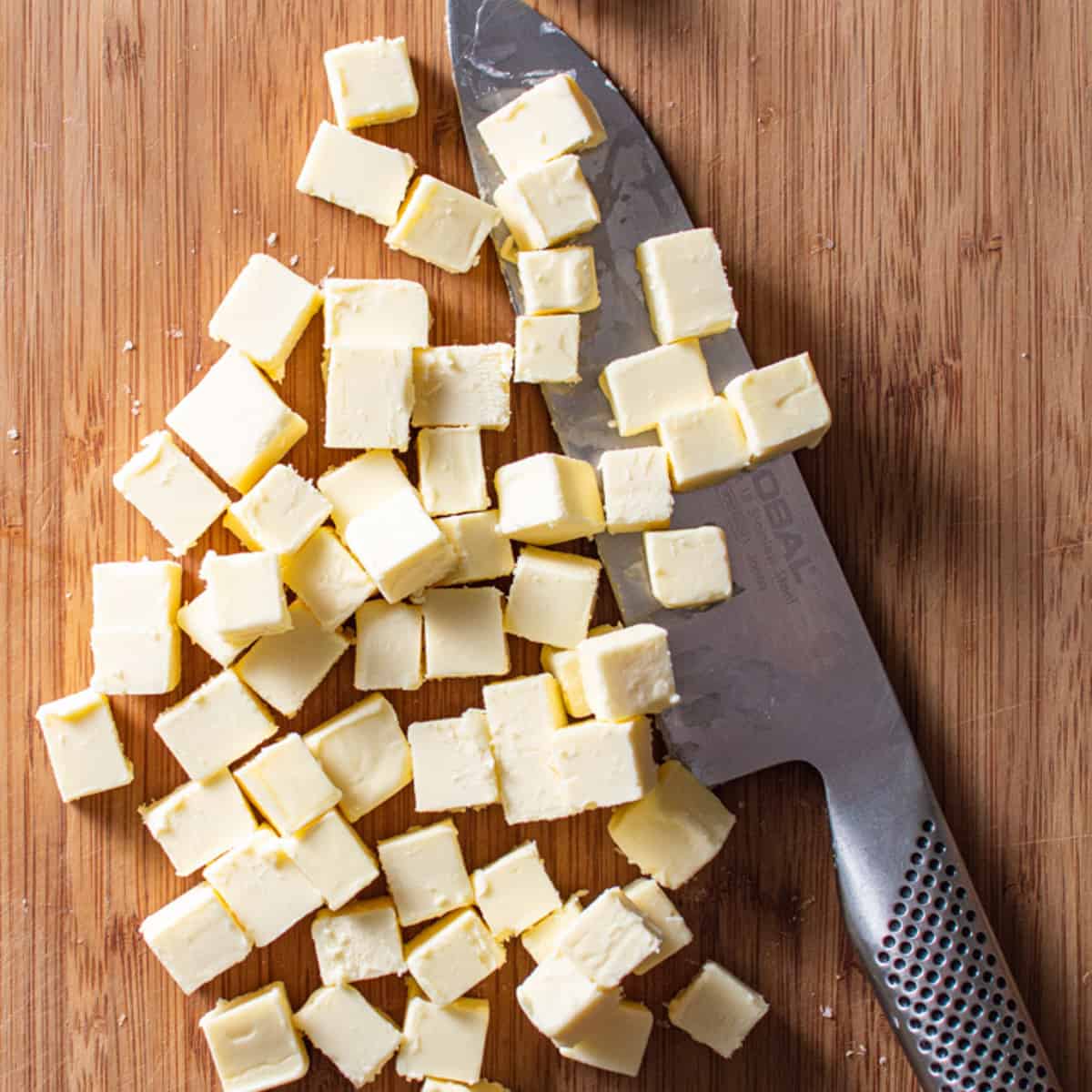 cubed butter with a chef's knife on wood board.