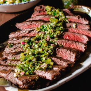 a sliced grilled flank steak with chimichurri sauce poured over it.