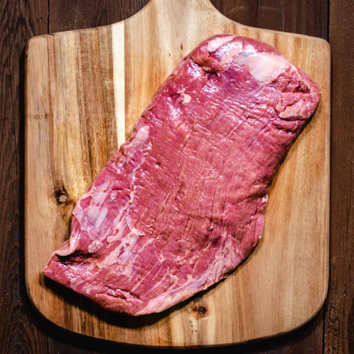 raw, whole flank steak on a wood board.