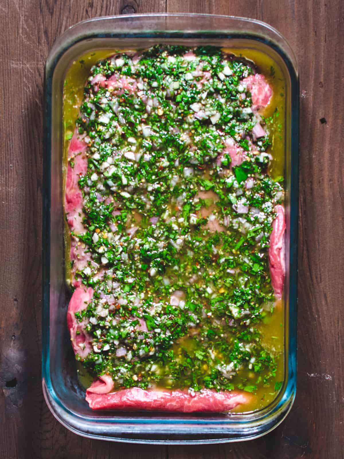 Flank steak marinating in a glass dish.