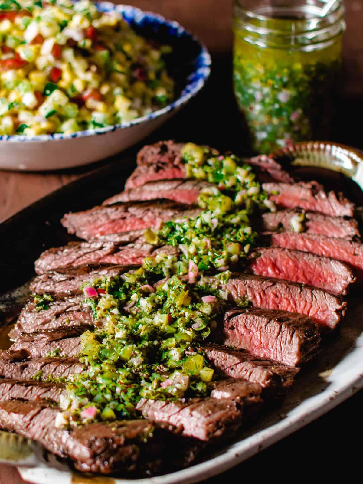 a sliced grilled flank steak with salsa verde poured over it.