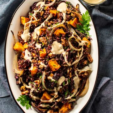 black rice salad on an oval platter drizzled with tahini dressing.