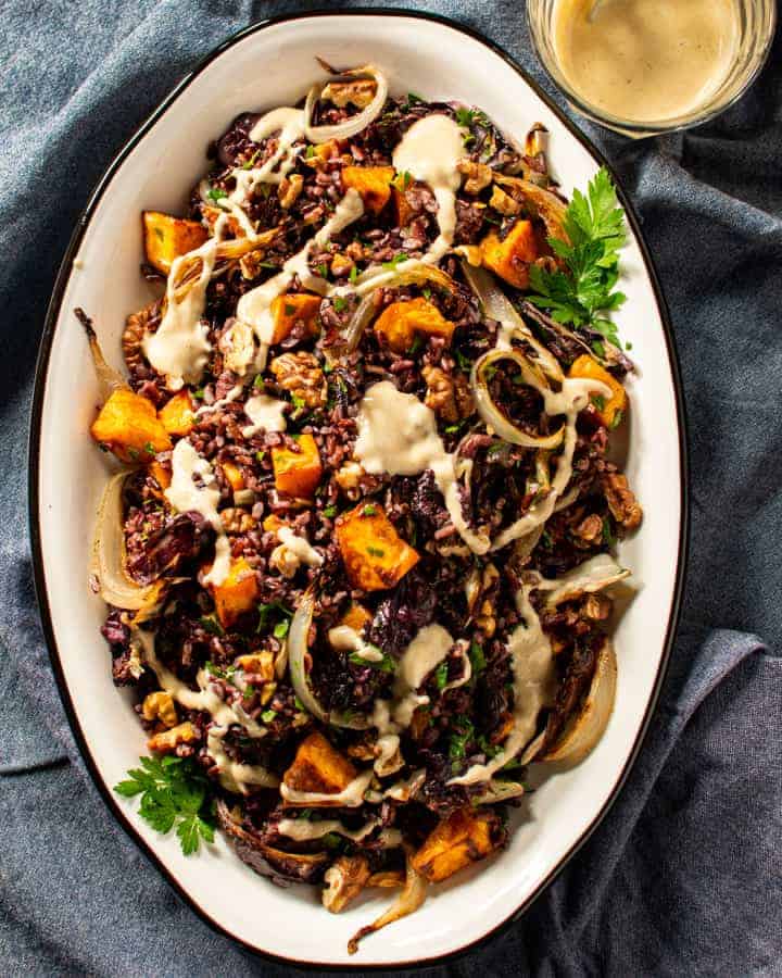 Black rice salad with roasted vegetables drizzled with dressing in white dish.