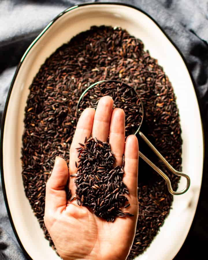 raw black rice in palm of hand over white dish