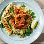 Grilled shrimp with coconut creamed corn on blue plate garnished with lime and zucchini.