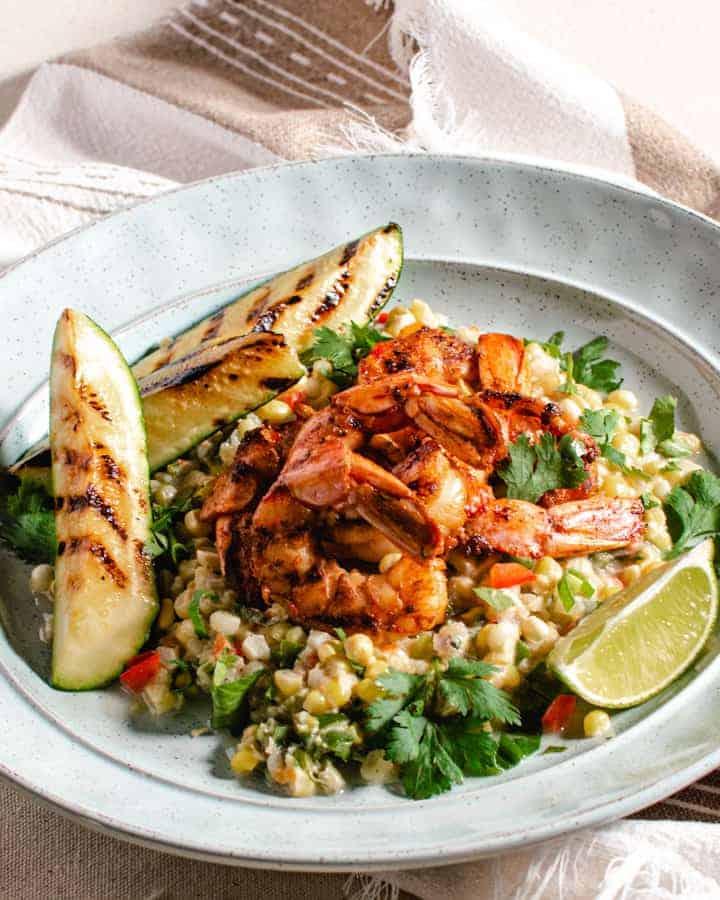 Grilled shrimp with coconut creamed corn on blue plate garnished with lime and zucchini