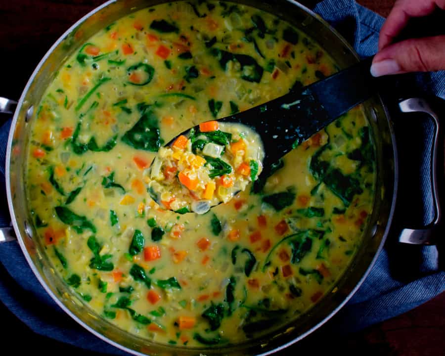 finished red lentil and vegetable soup in pot with black spoon