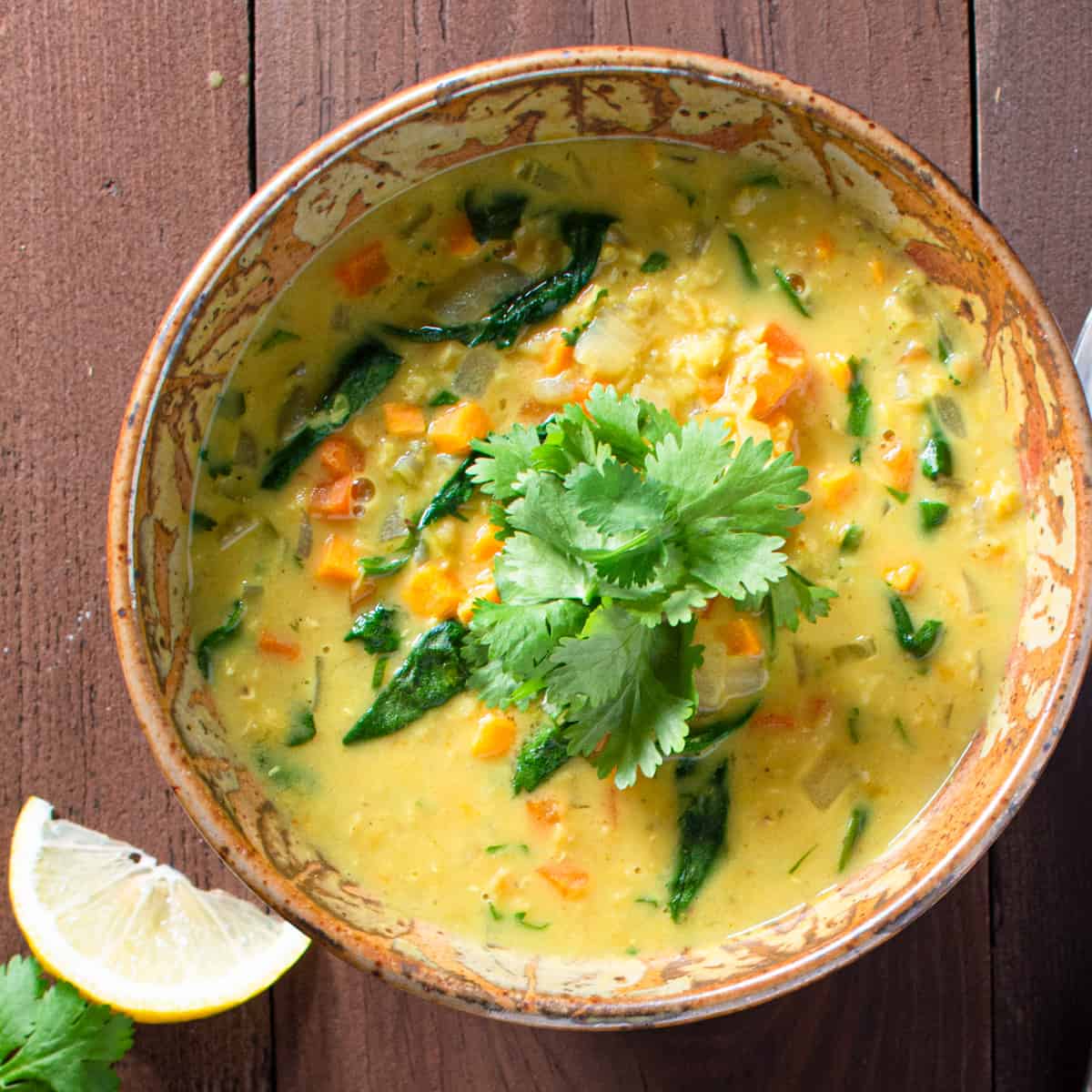 one bowl of red lentil and vegetable soup with lemon slice and cilantro.