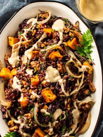 black rice salad on an oval platter garnished with tahini dressing.