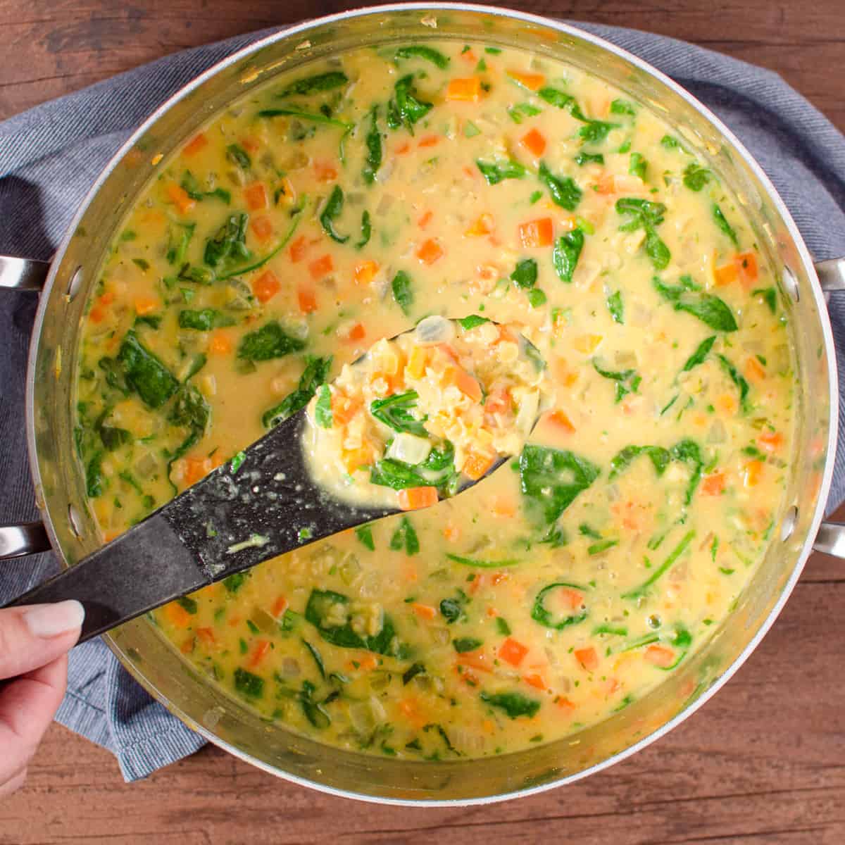 red lentil soup in a soup pot with a hand holding a spoonful.