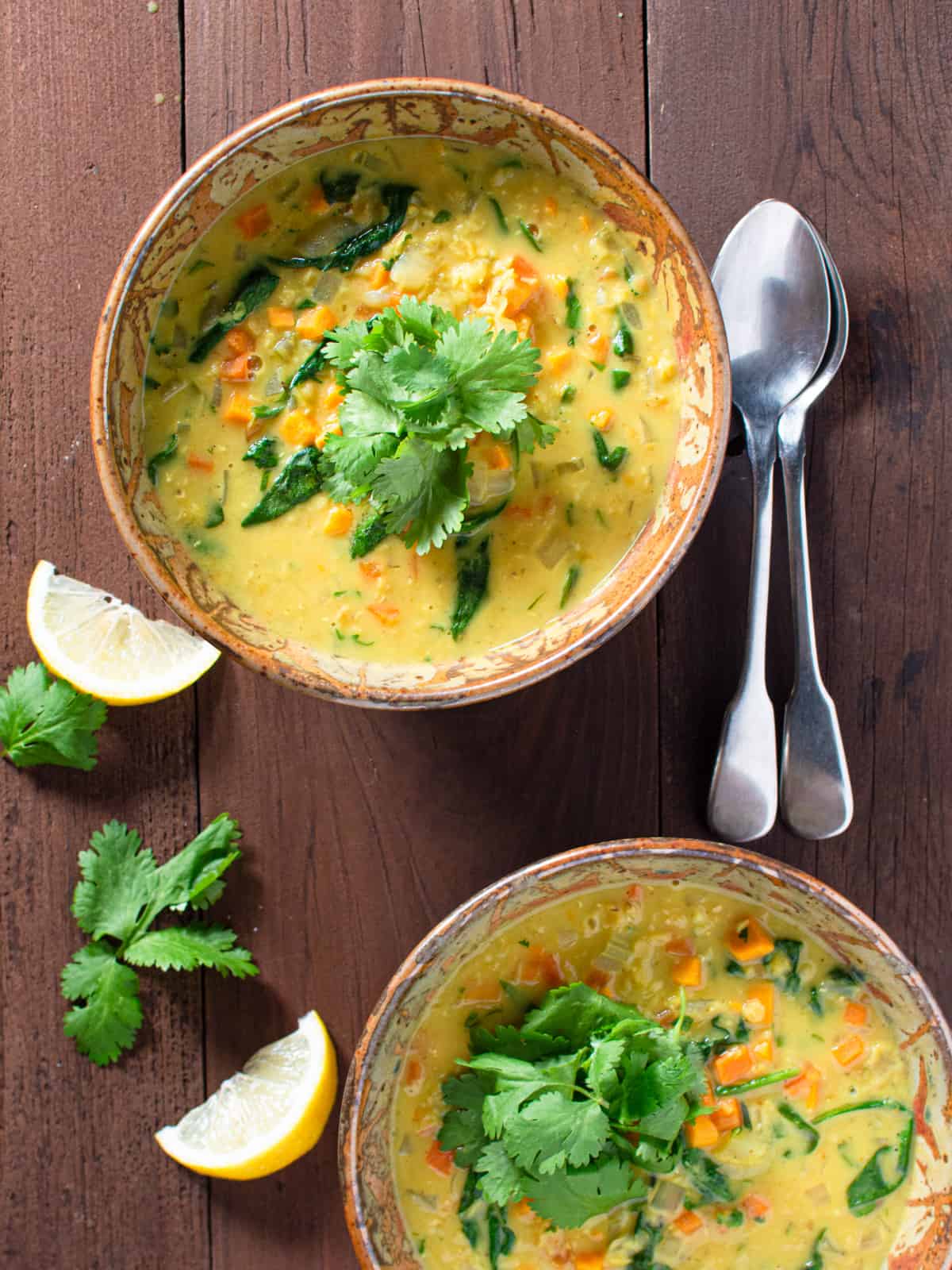 2 bowls of red lentil soup with spoons, lime and cilantro on the side. 