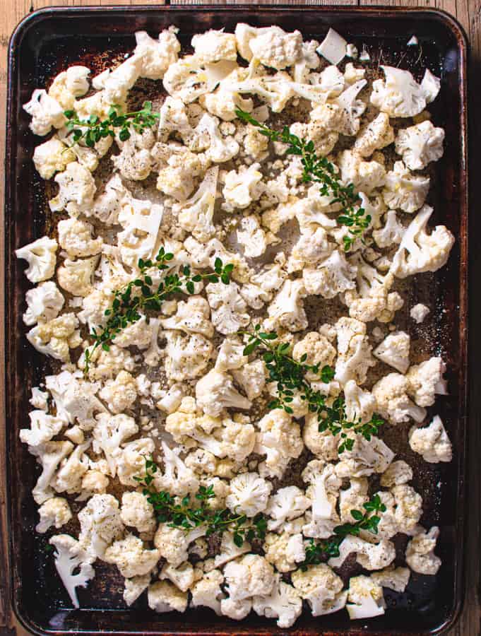 cut up cauliflower on baking tray with fresh thyme before baking