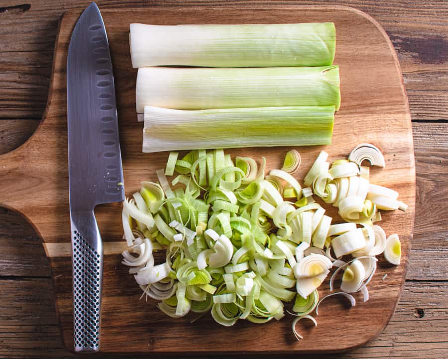 sliced leeks on wood cutting board with chef's knife