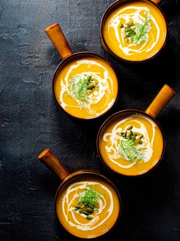 four bowls of butternut squash fennel and apple soup on a black background