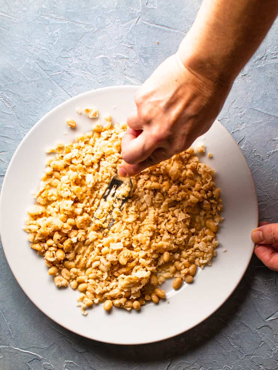 white beans being mashed on a plate with fork