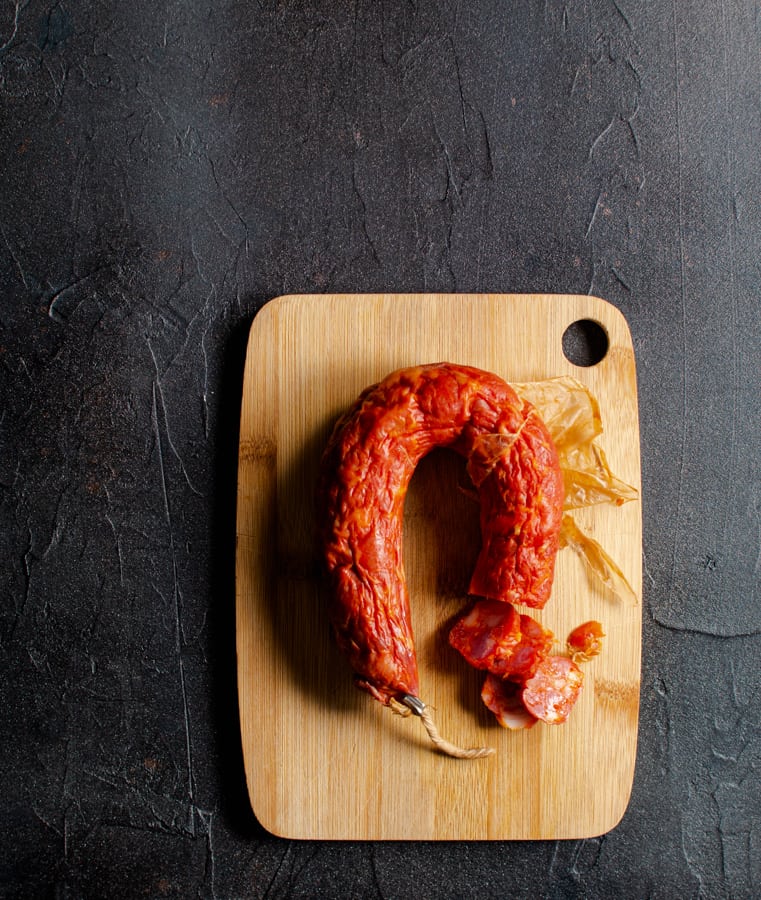 Spanish chorizo sausage on small board with black background