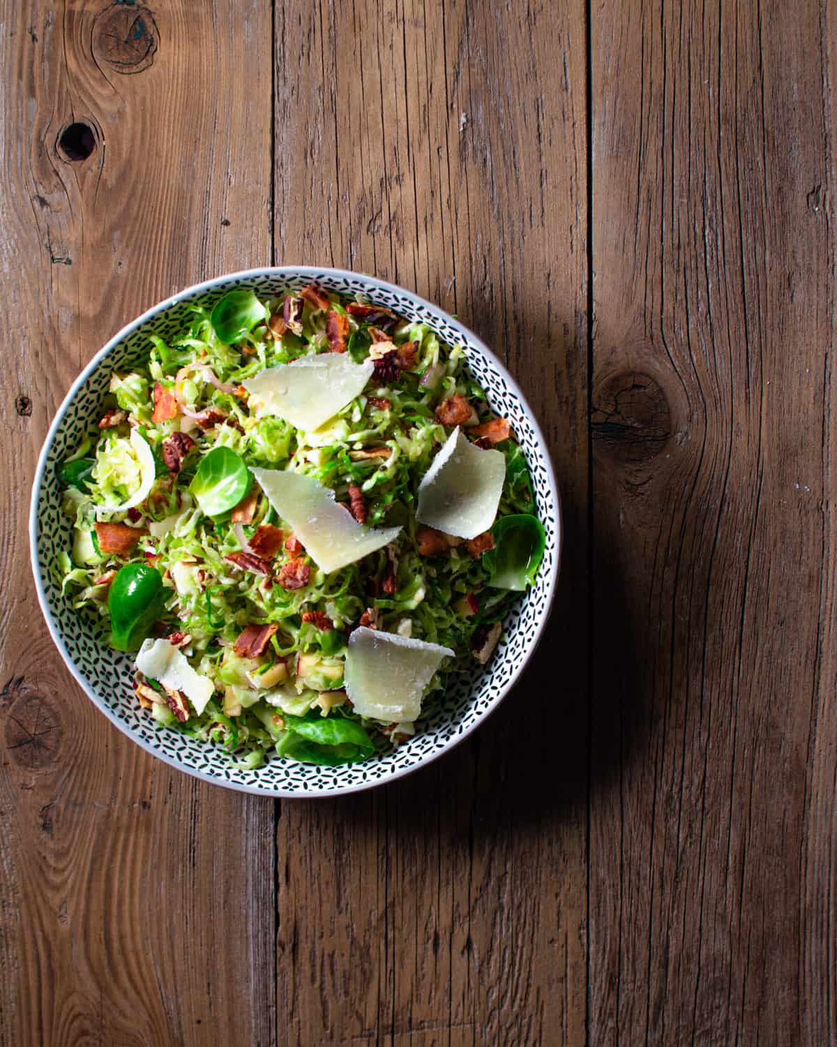 Brussels sprouts slaw in a white bowl on a wood background.