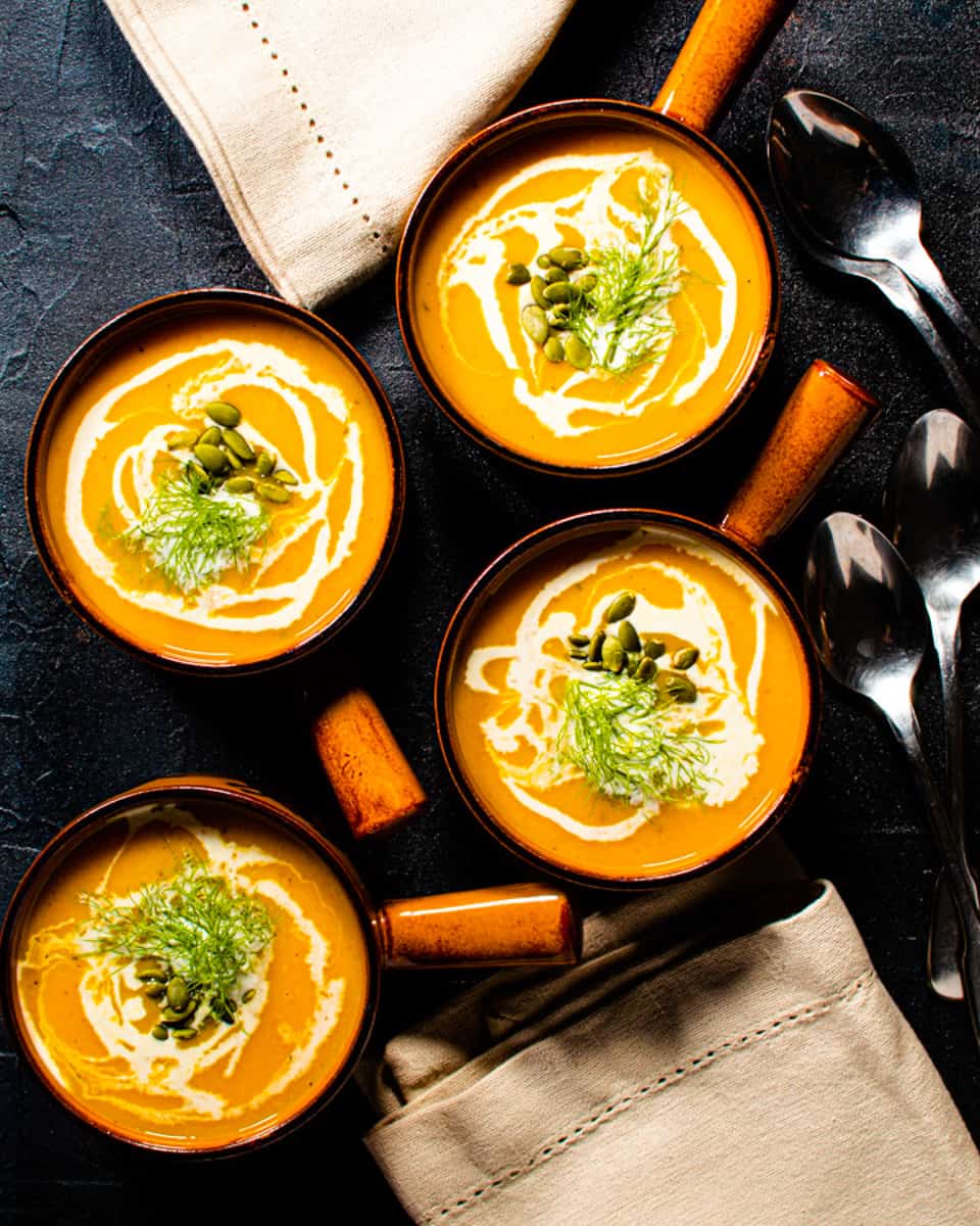 4 small bowls of butternut squash soup garnished with plain yogurt and fennel fronds. 