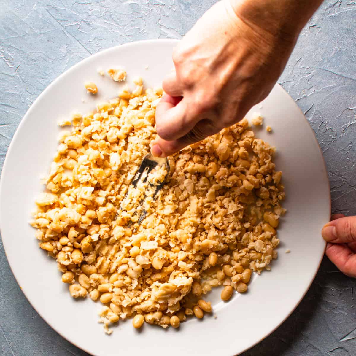 white beans being mashed on a plate with fork.