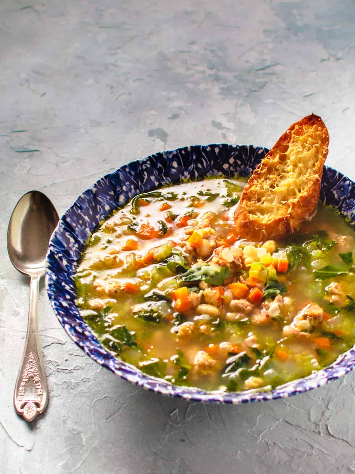 bowl of bean sausage and arugula soup in blue bowl.