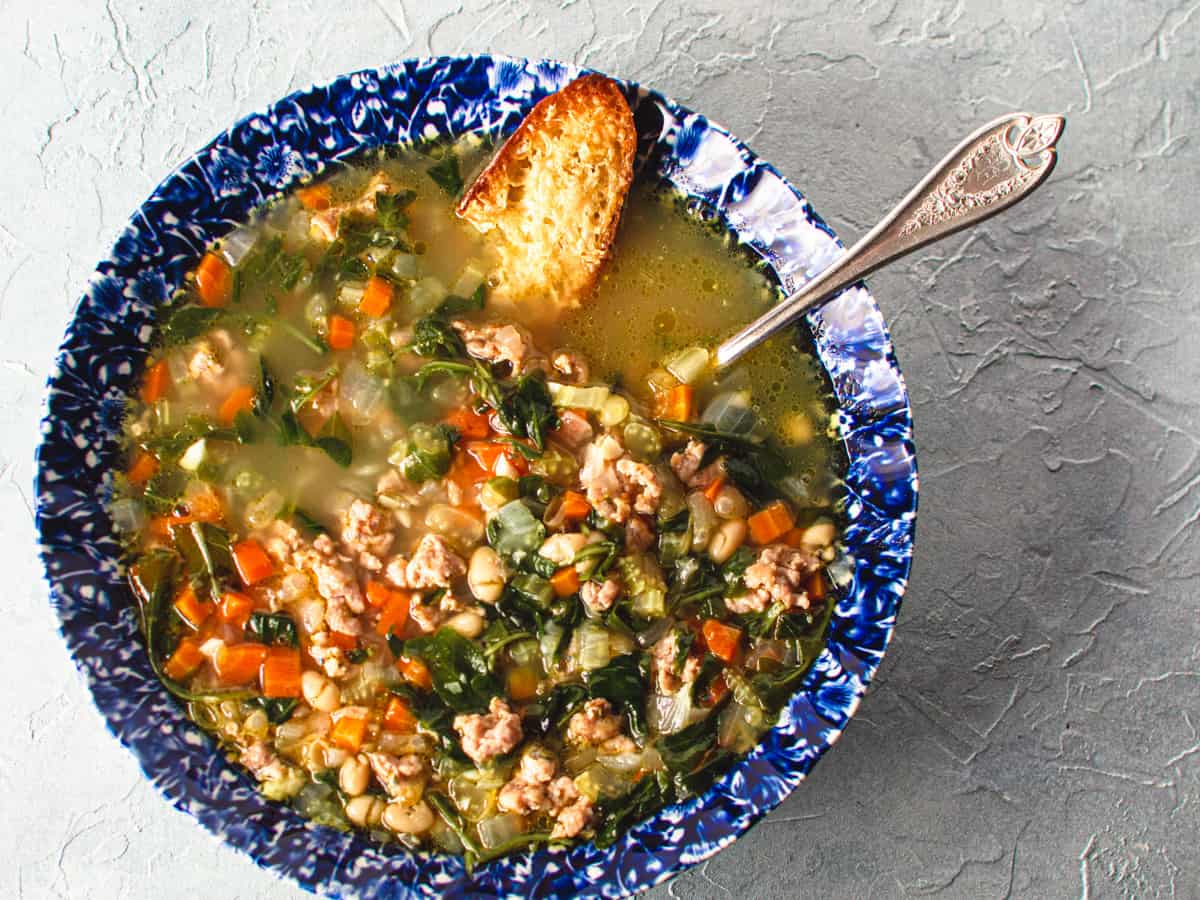 bowl of bean sausage and arugula soup in blue bowl with parmesan crostini.