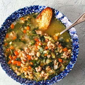 bowl of bean sausage and arugula soup in blue bowl with parmesan crostini.