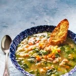 white bean sausage and arugula soup in blue bowl with Parmesan crostini and spoon