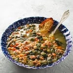 white bean sausage and arugula soup in blue bowl with Parmesan crostini and spoon