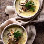 2 bowls of creamy chicken mushroom soup on a natural linen napkin garnished with fresh dill