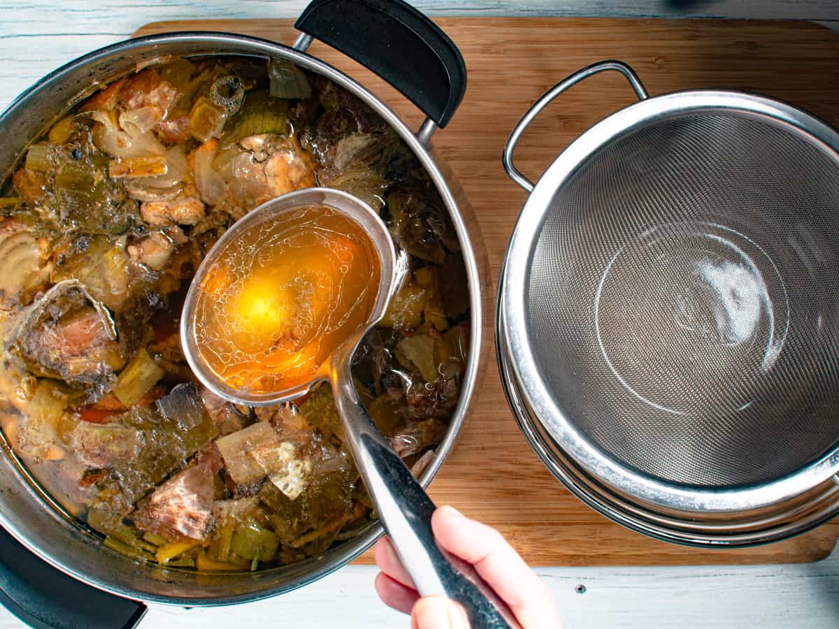 finished pot of chicken stock being strained into a bowl.