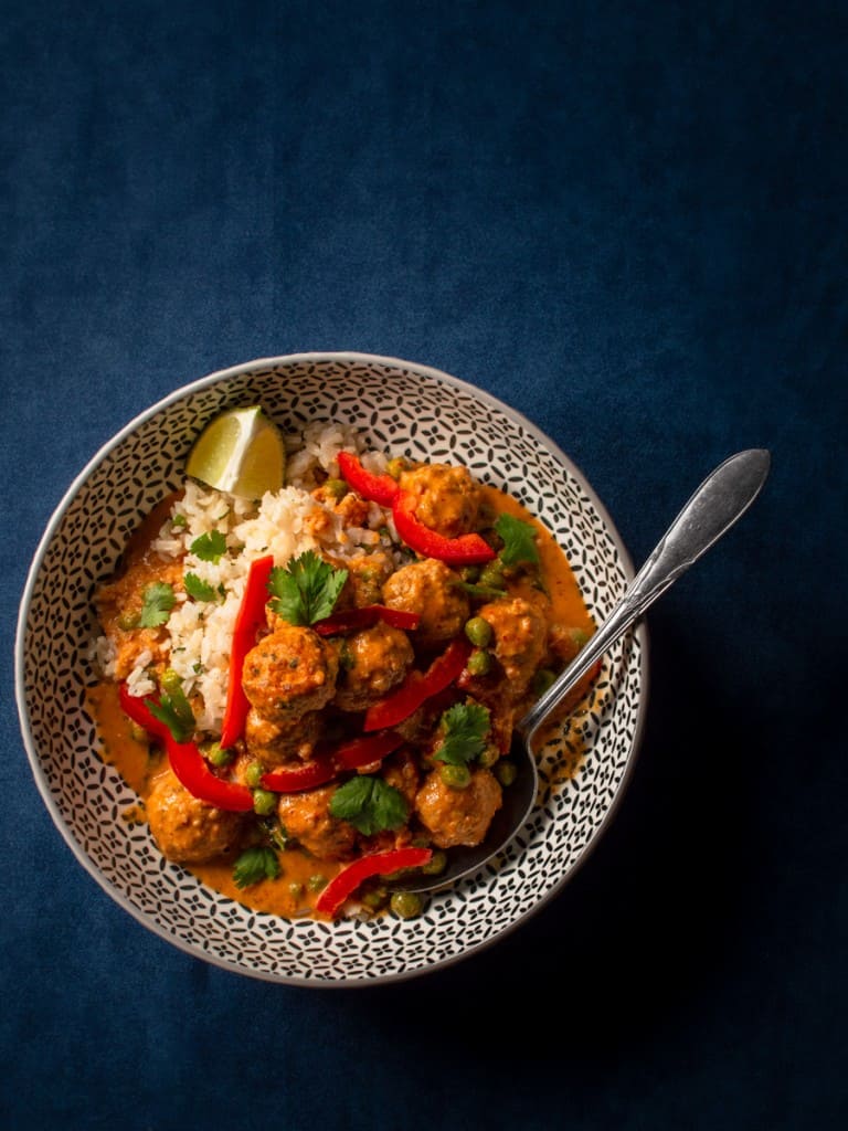 single bowl of thai meatballs with a spoon and lime garnish